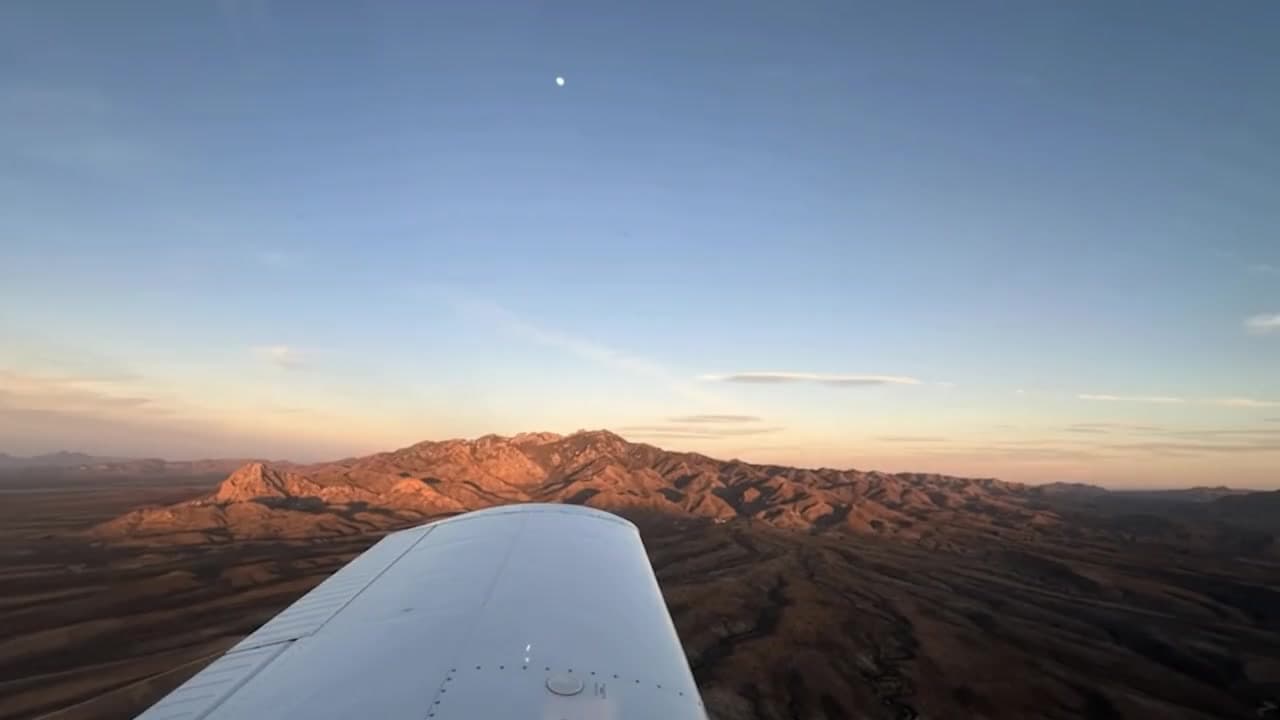 A training aircraft's wing over desert mountains glowing at sunset