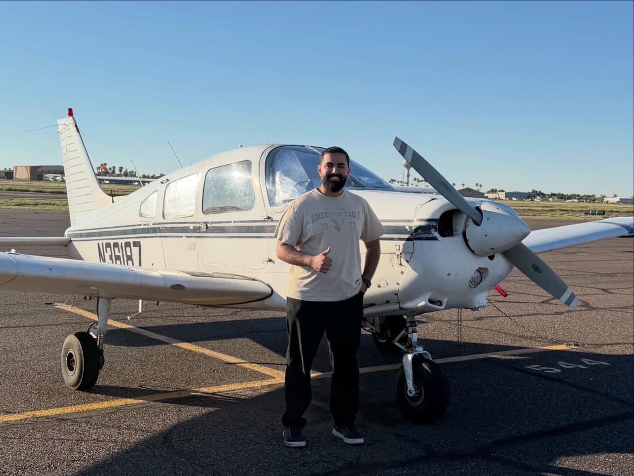 A Falcon Field student giving a thumbs-up beside a Piper training aircraft