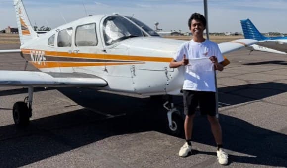 A smiling Falcon Field student beside a Piper training aircraft on the ramp